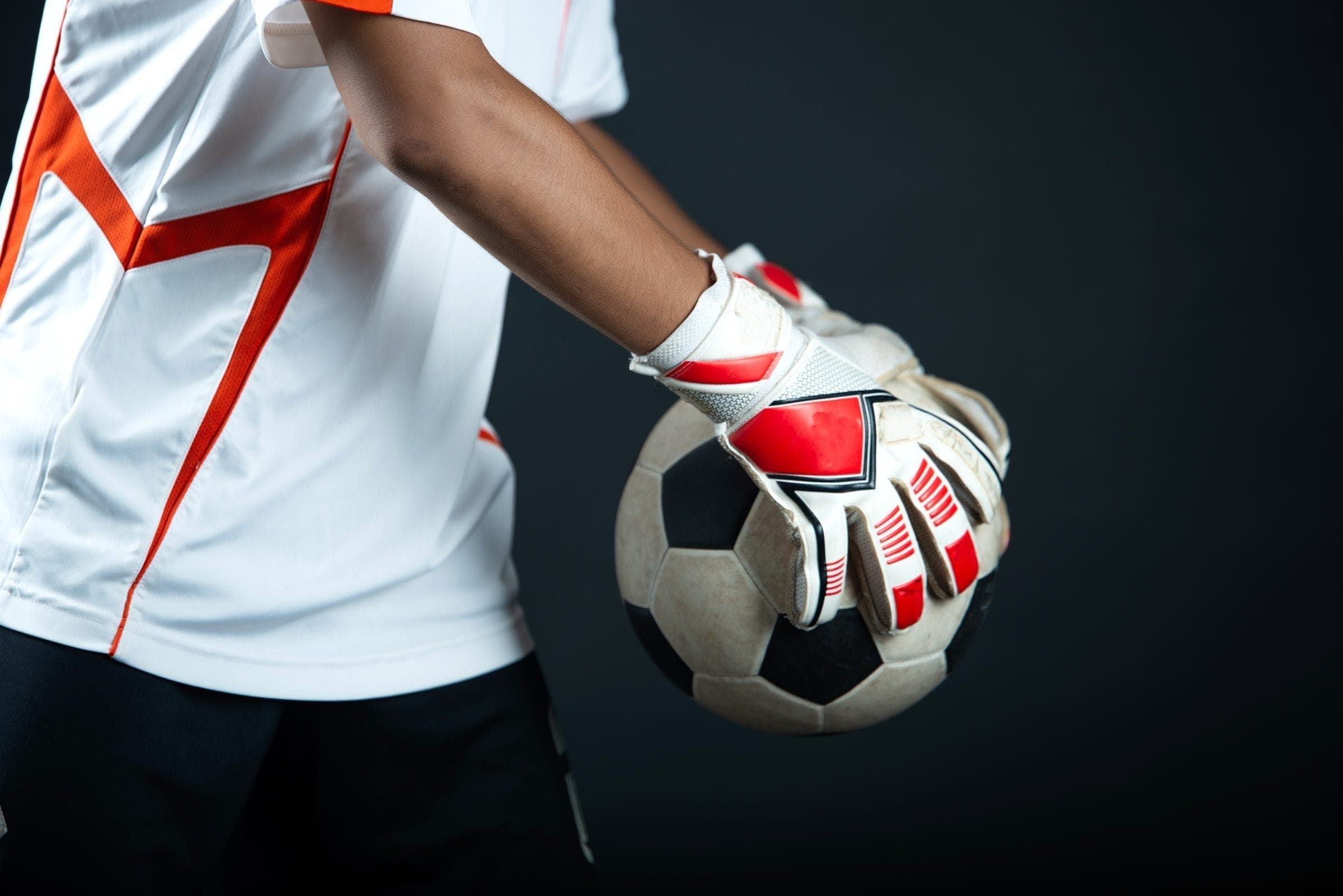 A goalkeeper holding a football, gloved hand resting on the ball